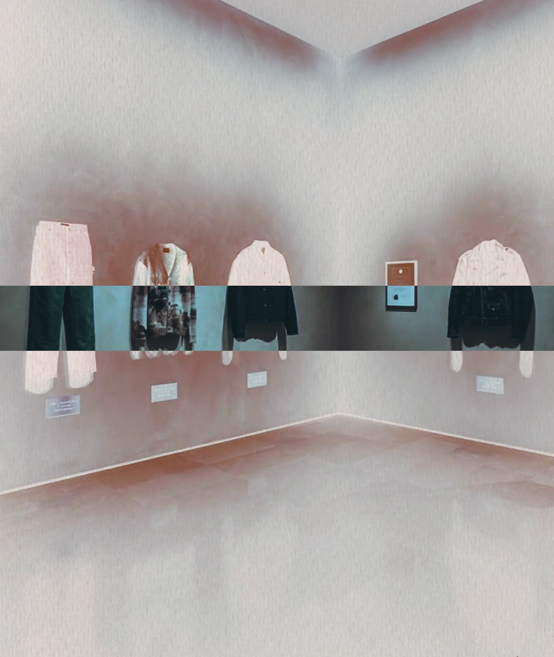 Installation study: garments hung around the corner of a pale gallery room, cut across by the house's inverted band.